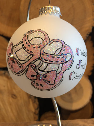 White Frosted Round Ornament depicting pink baby sandals with inscription "Baby's first Christmas" painted in swarovski crystals